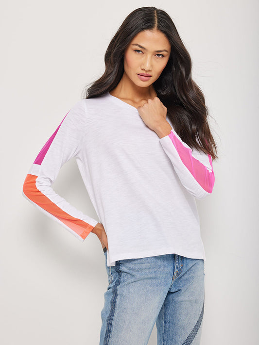 Model posing in a Lisa Todd Mesh On Long Sleeve Crew in White shirt with neon mesh pink and orange sleeve accents and blue jeans.