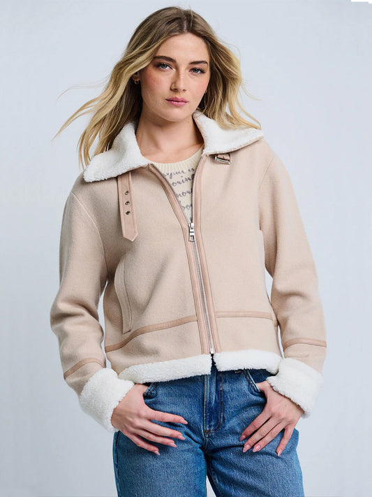 A woman wearing the Lisa Todd Moto Jacket With Sherpa Trim in Latte/Winter and blue jeans stands against a plain light background.