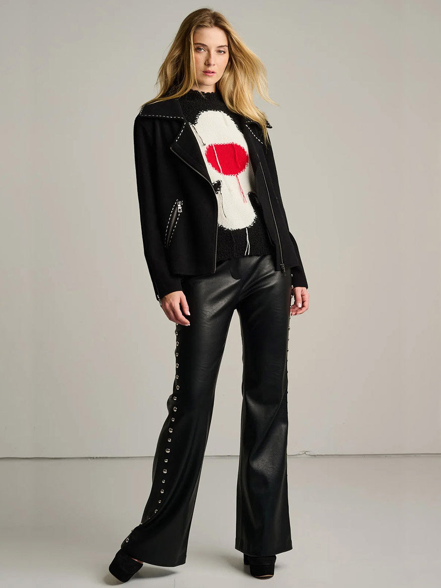 A person wearing a black Lisa Todd Moto Stitch Jacket with white contrast stitching over a graphic sweater and black trousers with side grommet detailing.