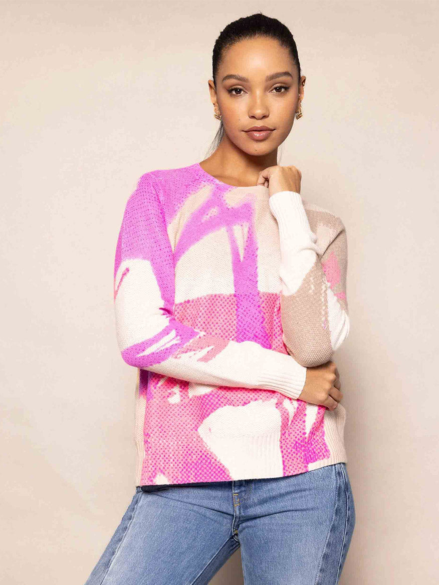 A person wearing the Lisa Todd Painter's Punch Sweater in Pink Pop with jeans stands against a beige background.