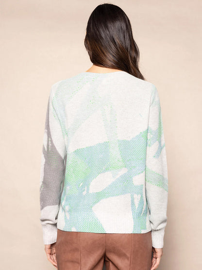 The individual is wearing the Lisa Todd Painter's Punch Sweater, featuring an artistic brush stroke design with abstract green and gray patterns, paired with brown pants, as they face away from the camera.