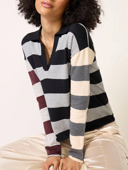 A person wears a Lisa Todd Perfect Pitch Collared V in Black/Grey, a long-sleeve, collared V-neck sweater featuring black, grey, cream, and maroon horizontal colorblock stripes.