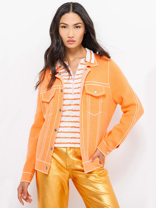 Woman posing in a Lisa Todd Pipe Dreamer jacket in Orange Flash with white trim, snap closures, a striped shirt, and metallic gold pants.