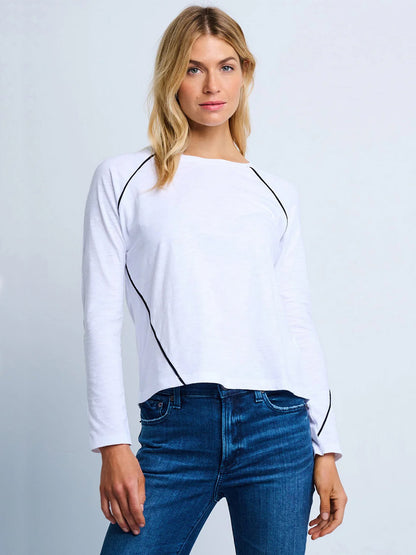 A woman wears the Lisa Todd Piping Hot Tee in White with black piping details and blue jeans, standing against a plain light background.