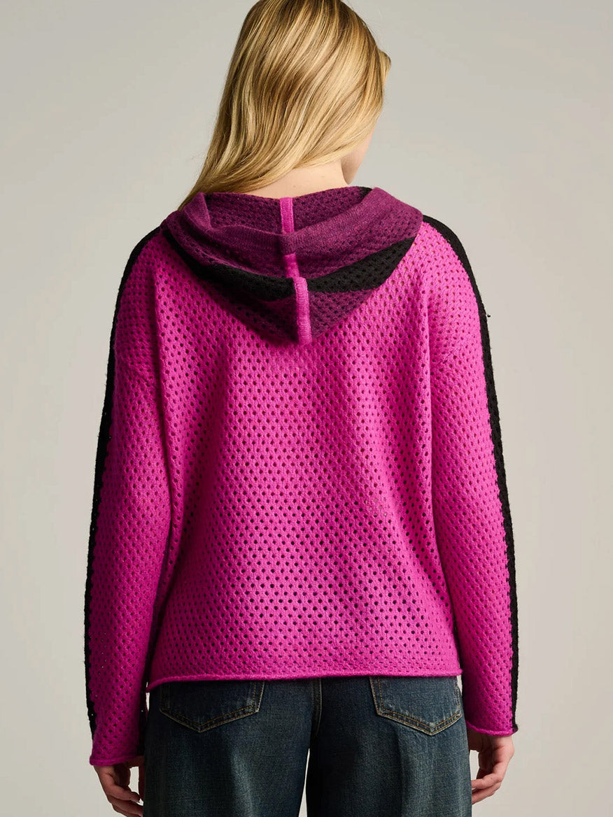 Person with long blonde hair wearing the Lisa Todd Pop Hoodie in Dark Berry Orchid, shown from the back. The oversized hoodie features a pink and black mesh texture and is paired with blue jeans.