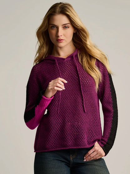 Woman wearing the Lisa Todd Pop Hoodie in Dark Berry Orchid—an oversized hoodie featuring a purple and black palette, perforated texture, and drawstrings, crafted from lightweight knit mesh stitch—standing against a plain light background.