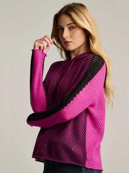 A person is wearing the Lisa Todd Pop Hoodie in Dark Berry Orchid, a bright pink long-sleeve mesh stitch top with black stripes down the sleeves, standing against a plain background.