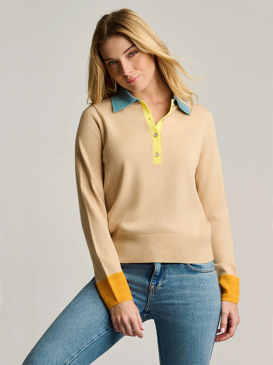 A woman wearing the Lisa Todd Pop Posh Cotton Cashmere Polo in Sable, featuring yellow contrast trim and pointelle cuffs, paired with blue jeans and standing against a plain background.