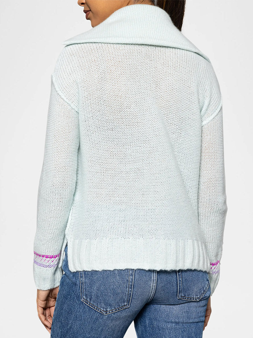 A person is wearing a chic Lisa Todd Powder Posh Sweater in Barely Blue, which features pink accents on the sleeves. They expertly pair it with classic blue jeans for a stylish and comfortable ensemble.