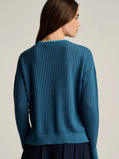 Woman with long brown hair shown from the back against a plain background, wearing the Lisa Todd Power Stitch Cotton Pullover in Steel Blue—a textured cotton pullover with subtle embroidered details—paired with a dark skirt.