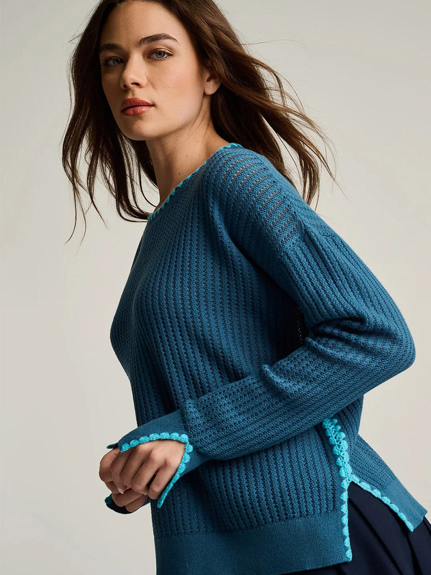 A woman poses sideways against a plain background wearing the Lisa Todd Power Stitch Cotton Pullover in Steel Blue, featuring textured knit cotton, light blue trim, and subtle novelty stitch accents.