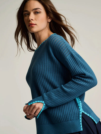 A woman poses sideways against a plain background wearing the Lisa Todd Power Stitch Cotton Pullover in Steel Blue, featuring textured knit cotton, light blue trim, and subtle novelty stitch accents.