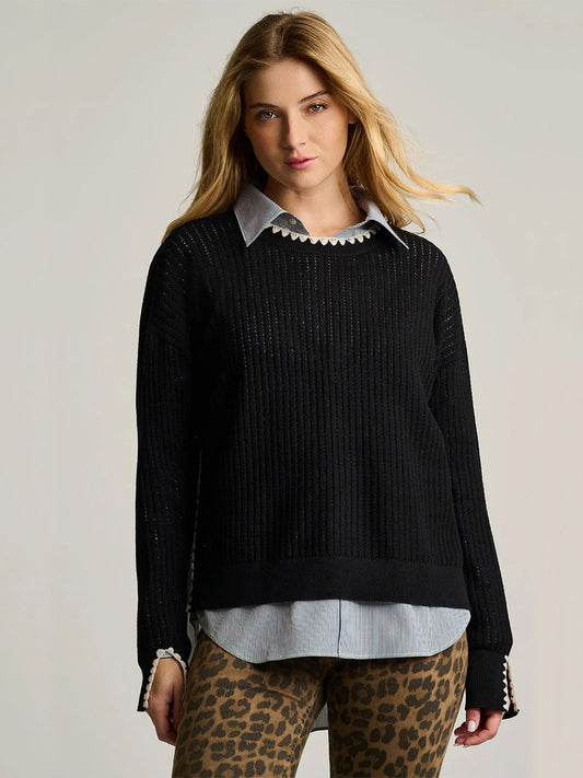 A woman with long blonde hair wears the Lisa Todd Power Stitch Cotton Pullover in Black over a collared shirt and leopard print pants, standing against a neutral background.