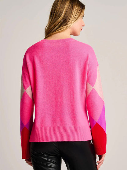 A blonde woman, shown from the back, wears the Lisa Todd Power Surge Sweater in Neon Pink with bold diamond sleeves and black leather pants.