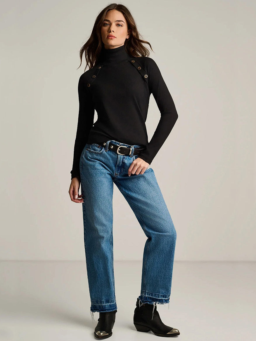 A black Lisa Todd Pure Pima Rib Turtleneck with button details at the shoulders, worn with blue jeans and black boots.
