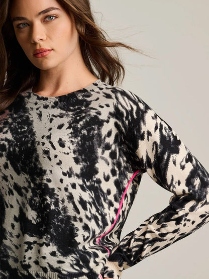 A woman wears the Lisa Todd Running Wild Cotton Sweater in Chocolate Feather—a relaxed fit, multicolor animal print style with pink trim, crafted from 100% cotton—standing against a plain light background.