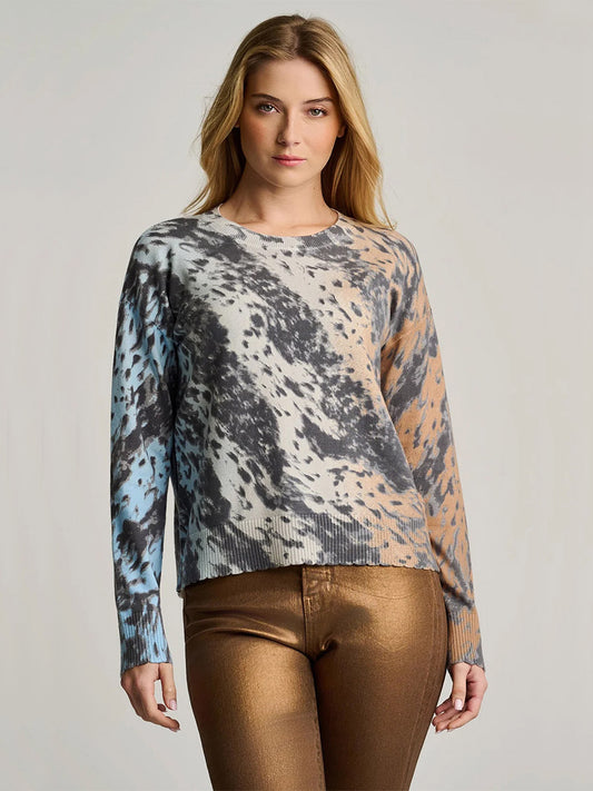 Woman wearing the Lisa Todd Running Wild Cotton Sweater in Ice Blue/Camel, featuring 100% cotton with a multicolored abstract pattern and relaxed fit, paired with metallic bronze pants and standing against a plain background.
