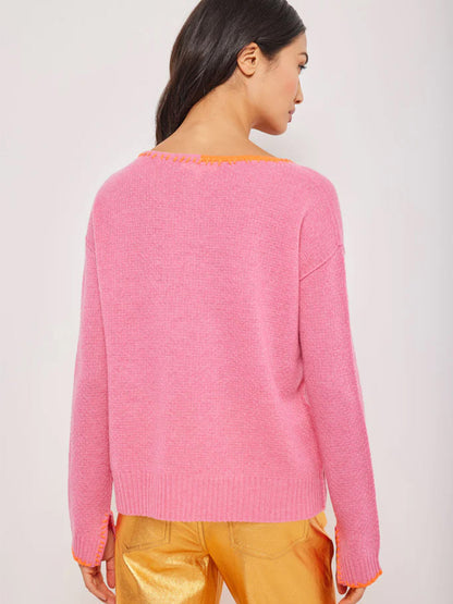 Rear view of a woman wearing a Lisa Todd Split Decision Sweater in Pink Punch with an orange-trimmed neckline, paired with shiny gold pants.