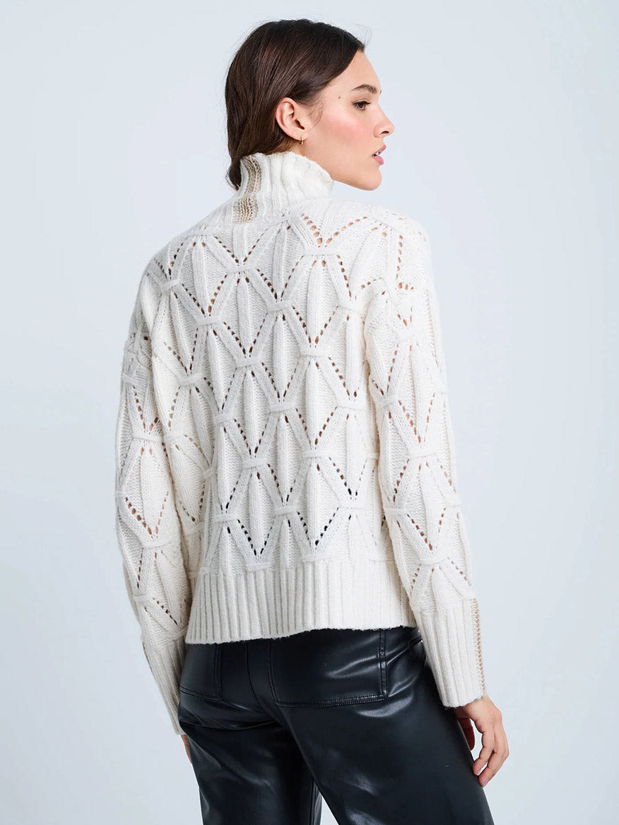 A woman is shown from the back wearing the Lisa Todd Stand Out Cable Turtleneck in Winter White with black leather pants.