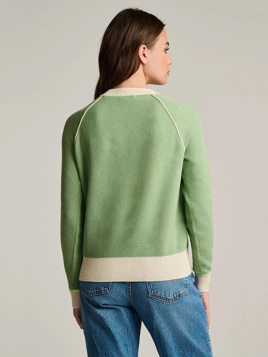 A person is shown from the back against a neutral background wearing the Lisa Todd Stitchin’ Cotton Cashmere Sweater in Sage, featuring cream trim, paired with blue jeans.
