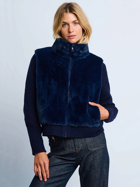 A woman wears the Lisa Todd Teddy Faux Fur Knit Jacket in Navy over a dark sweater and jeans, standing against a light background.