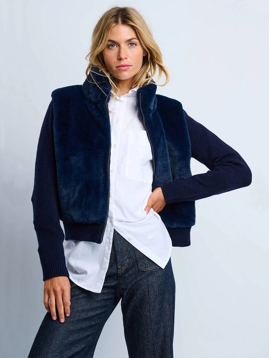 A woman wears the Lisa Todd Teddy Faux Fur Knit Jacket in Navy over a white button-up shirt and dark jeans, standing against a plain light background.
