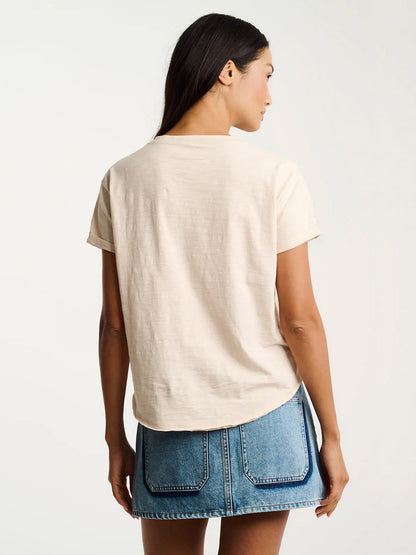 Woman stands with her back to the camera, wearing the Lisa Todd What The Flock Tee in Crystal Sand and a blue denim skirt with large back pockets against a plain background.