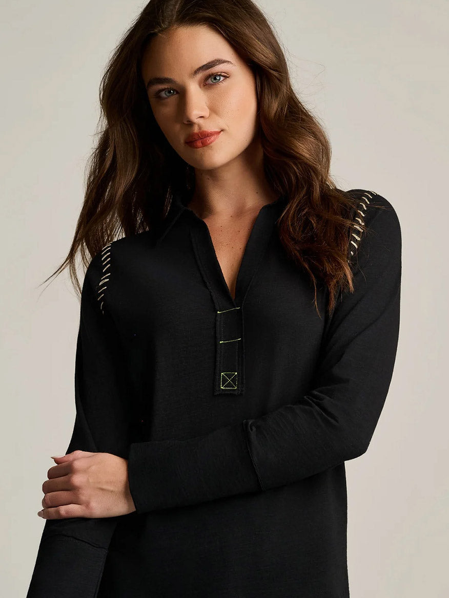 A woman with long brown hair is wearing the Lisa Todd Whipster Cotton T-Shirt in Black, a relaxed-fit, long-sleeved cotton top with subtle stitching detail on the shoulders, standing against a plain background.
