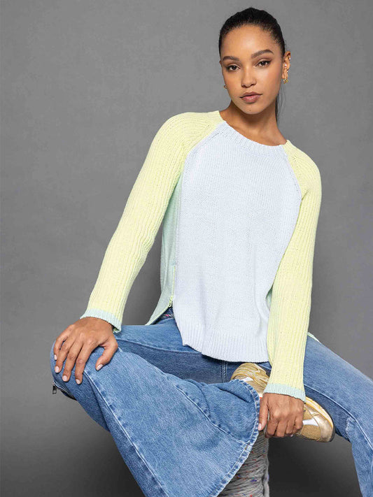 A person wearing the Lisa Todd Zip Me Sweater in Ice Combo paired with flared jeans sits against a gray background.