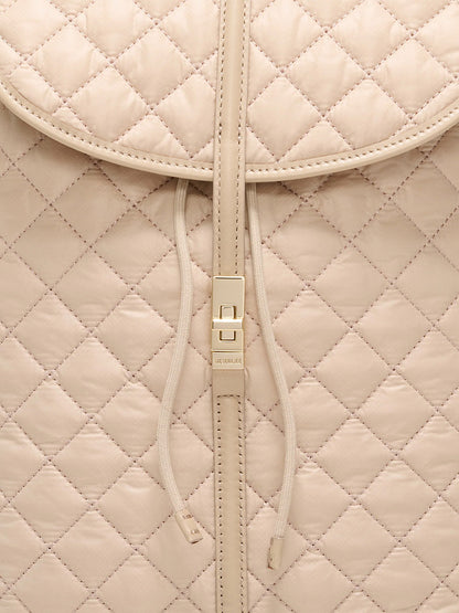 Close-up of the MZ Wallace Astor Backpack in Buff Oxford, featuring beige quilted leather, a drawstring closure, and a gold-tone central buckle that highlights its luxe detailing.
