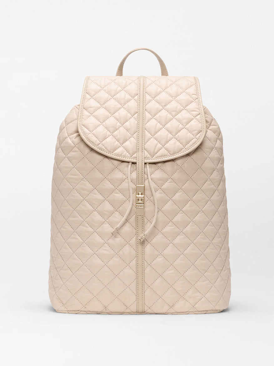 The MZ Wallace Astor Backpack in Buff Oxford is a beige quilted laptop backpack with a flap closure, drawstring, and top handle, shown against a plain white background.