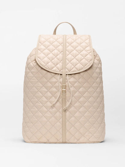 The MZ Wallace Astor Backpack in Buff Oxford is a beige quilted laptop backpack with a flap closure, drawstring, and top handle, shown against a plain white background.