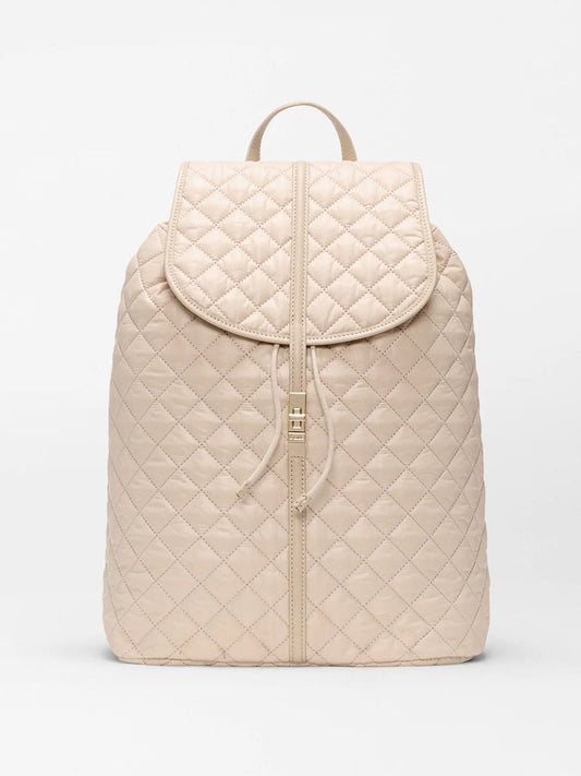 The MZ Wallace Astor Backpack in Buff Oxford is a beige quilted laptop backpack with a flap closure, drawstring, and top handle, shown against a plain white background.