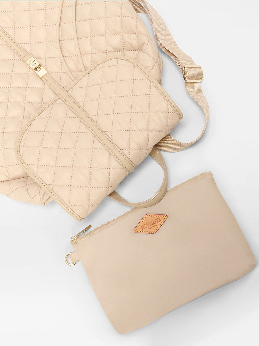 The MZ Wallace Astor Backpack in Buff Oxford, shown on a white background, features a quilted beige design with gold accents and comes with a matching beige pouch featuring a small leather patch.