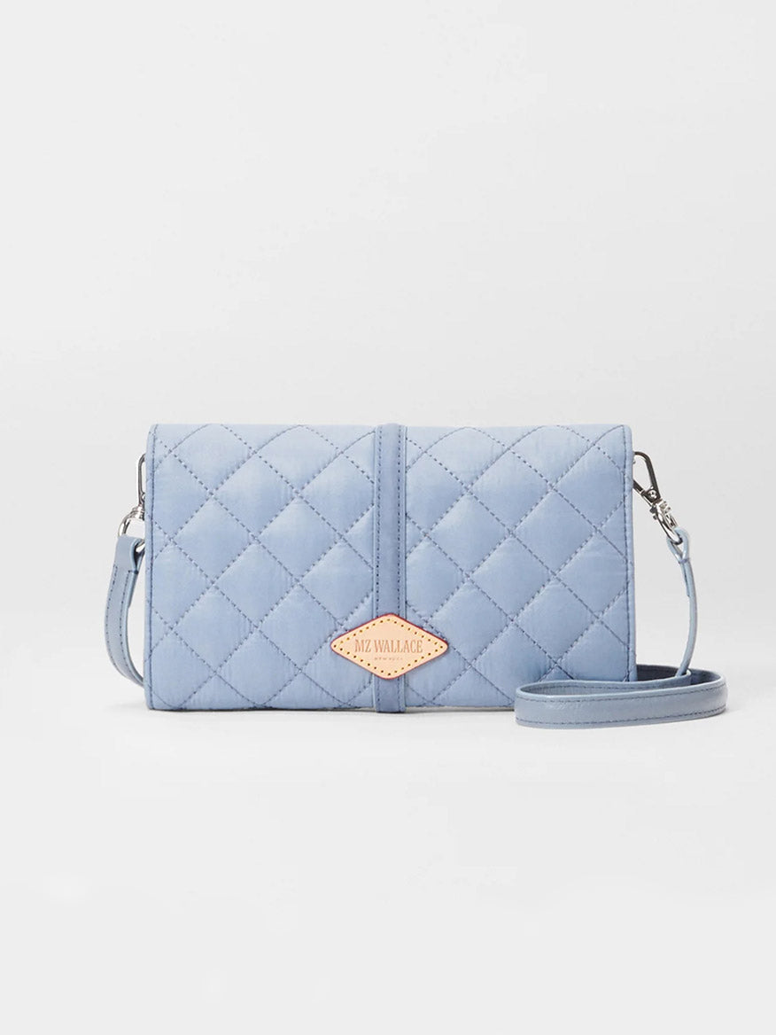 The MZ Wallace Astor Convertible Crossbody in Stone Blue Oxford is a quilted bag featuring an Italian leather strap and a small logo patch on the front, part of the elegant Astor Collection.