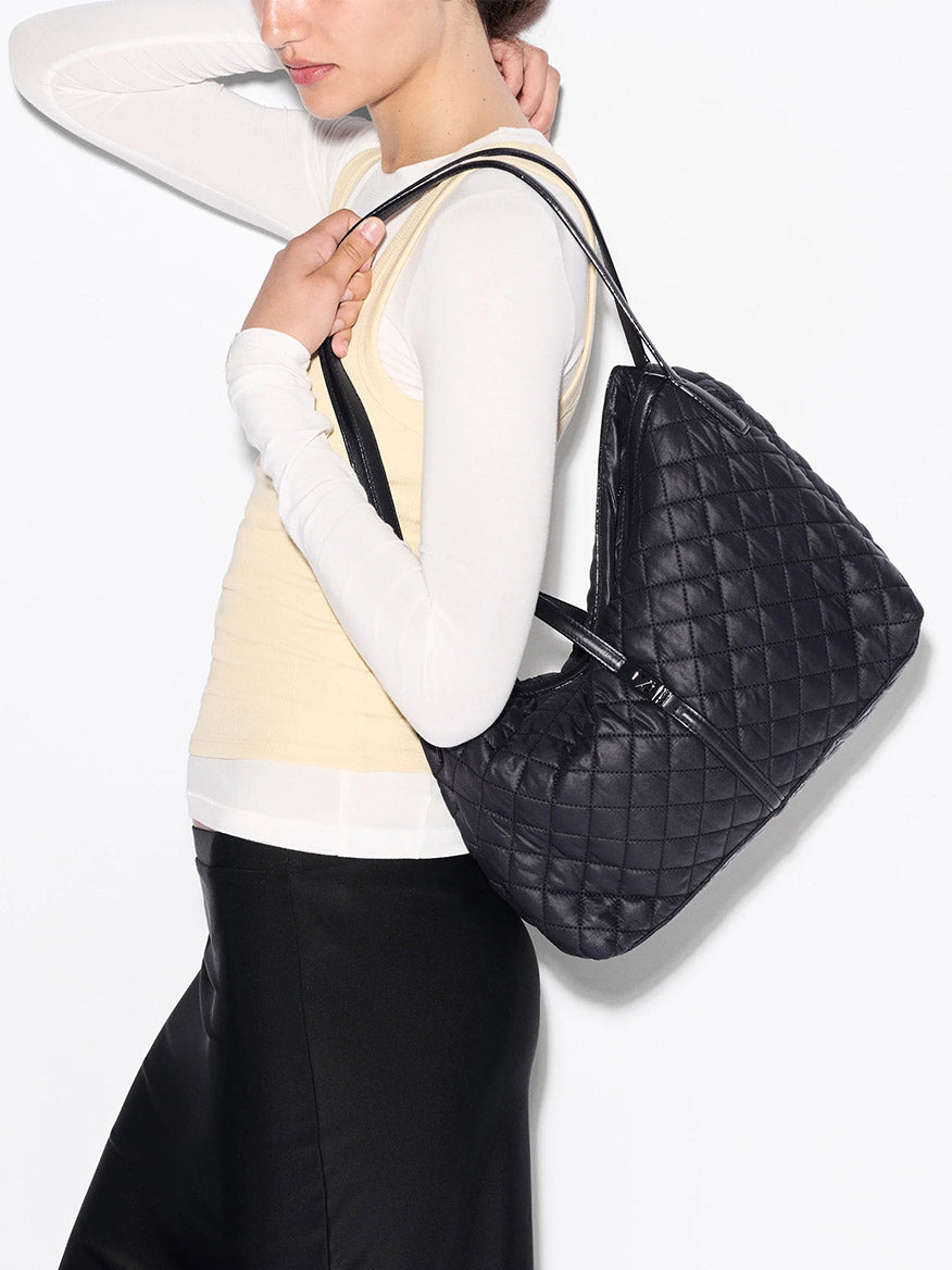 A person wearing a light yellow top and black skirt carries the MZ Wallace Astor East West Tote in Black Oxford.
