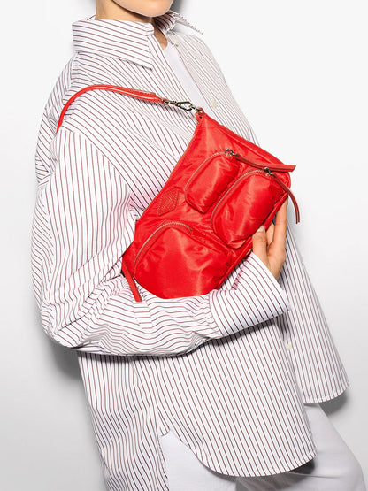 A person in a pinstripe shirt holds an MZ Wallace Chelsea Petite Shoulder Bag in Bright Cherry Bedford against a plain background, featuring vibrant red quilting and Italian leather trim.