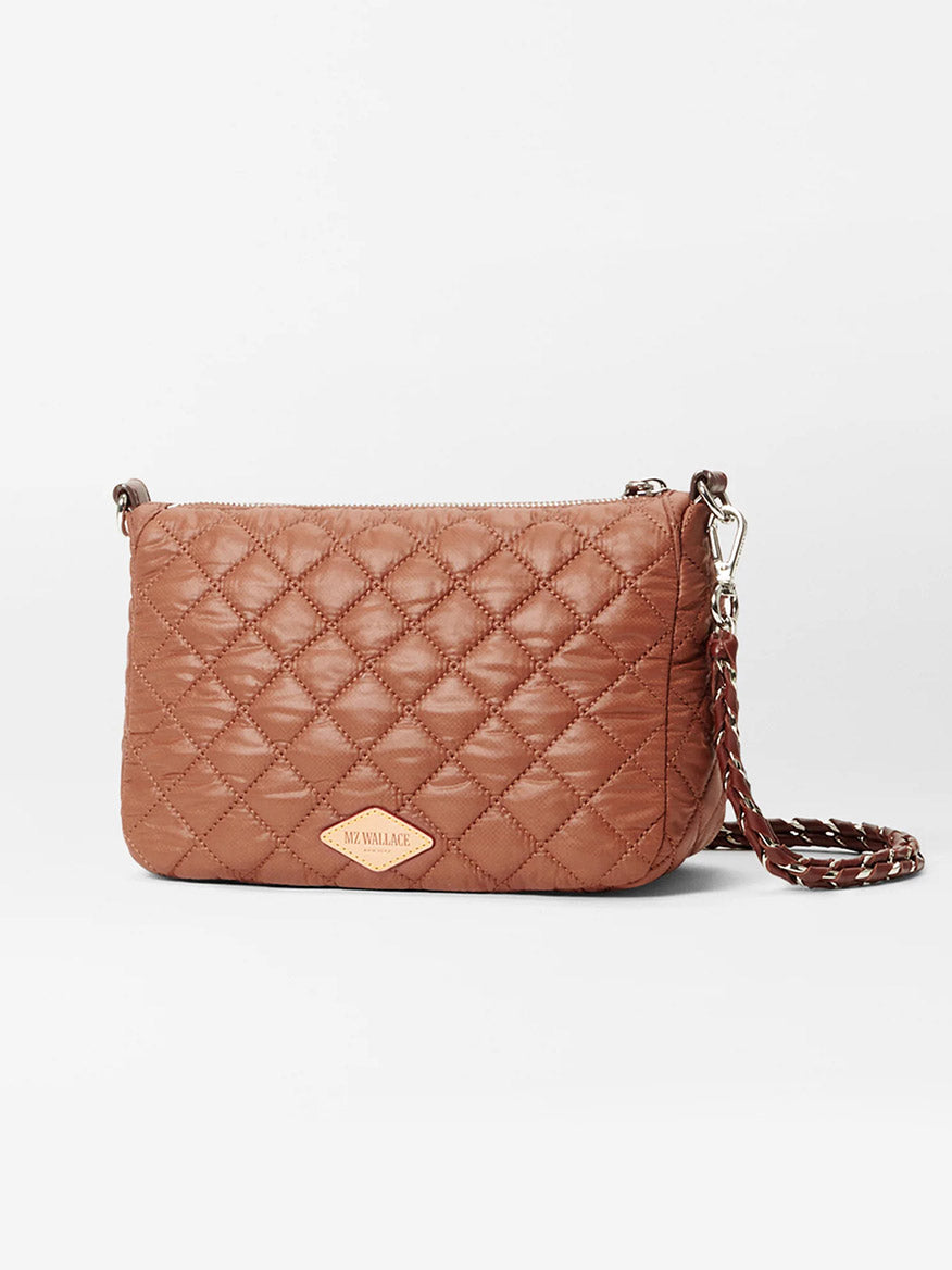 The MZ Wallace Crosby Ella Crossbody in Terracotta Oxford is a brown quilted bag with a zipper closure, Italian leather trim, and a braided adjustable shoulder strap. It features a small rectangular leather logo patch on the front.