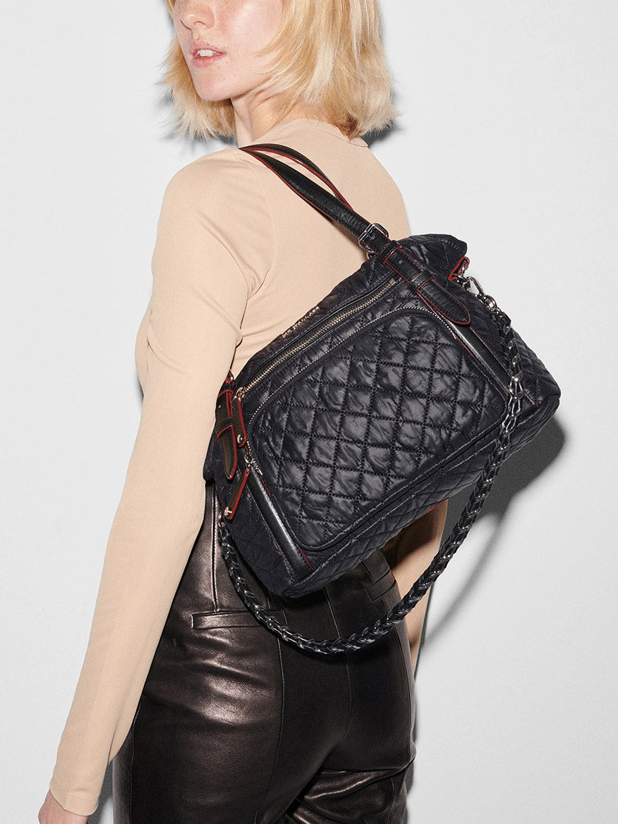 A woman with blonde hair wears a beige long-sleeve top, black leather pants, and carries the MZ Wallace Crosby Everywhere Tote in Black Oxford over her shoulder.