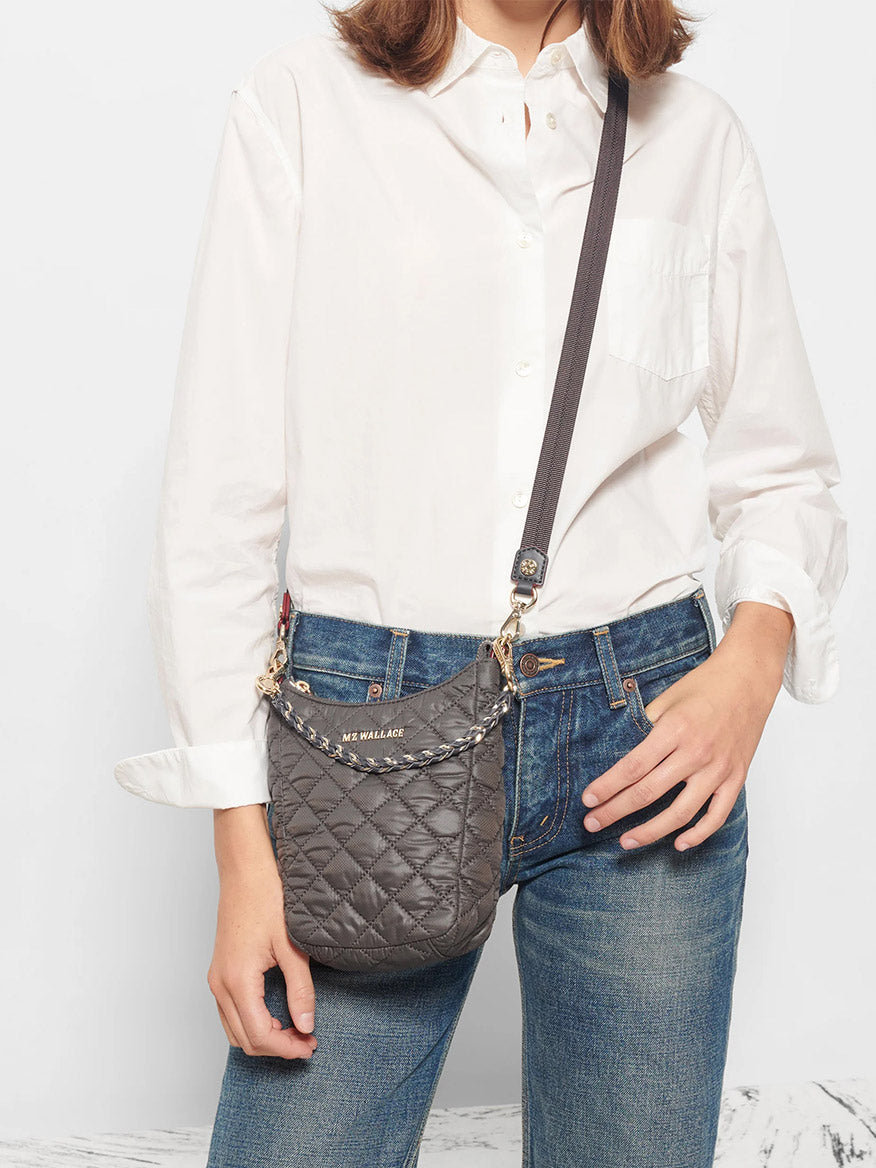 Person wearing a white shirt and blue jeans, carrying an MZ Wallace Crosby Go in Magnet Oxford with an adjustable crossbody strap.