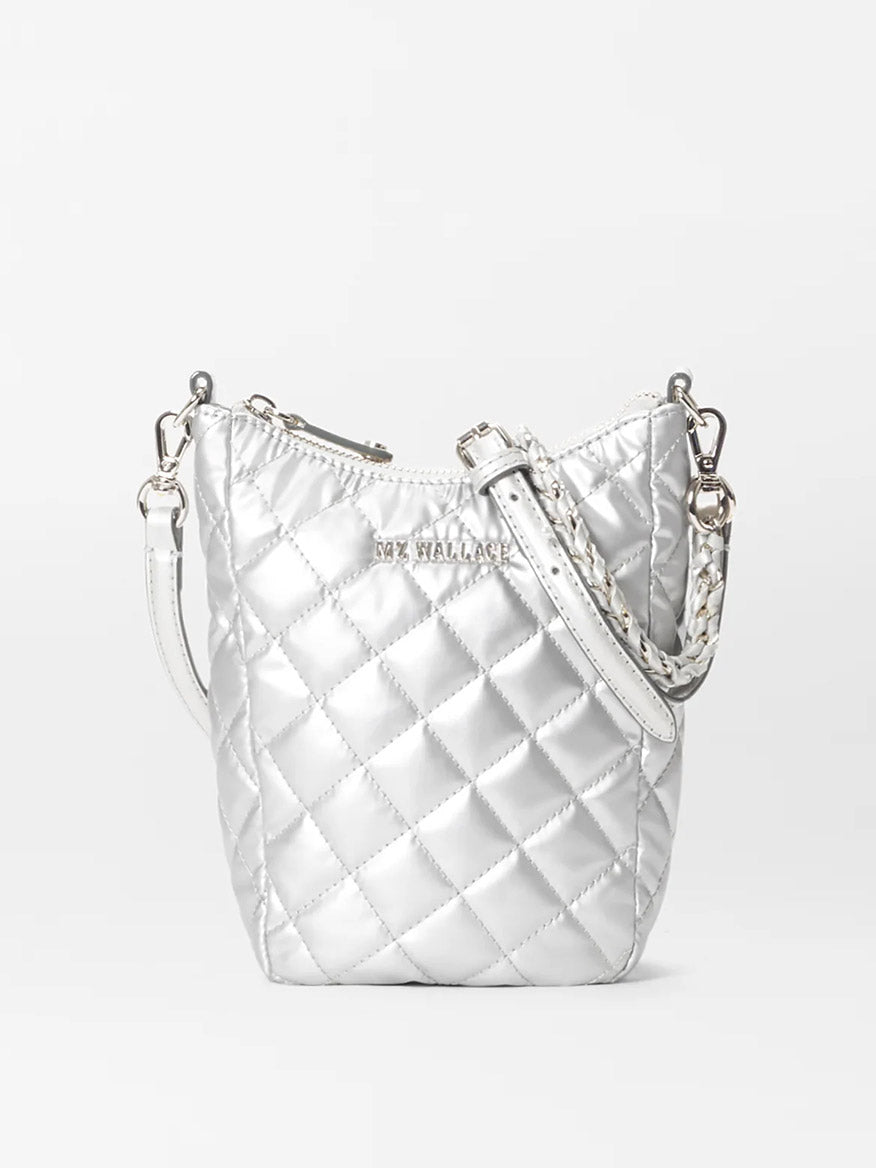 The MZ Wallace Crosby Go in Matte Silver Oxford is a small quilted bucket bag made from metallic silver fabric, featuring a braided strap and a zipper closure.