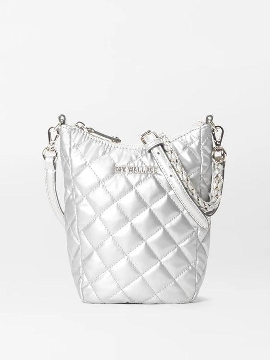 The MZ Wallace Crosby Go in Matte Silver Oxford is a small quilted bucket bag made from metallic silver fabric, featuring a braided strap and a zipper closure.