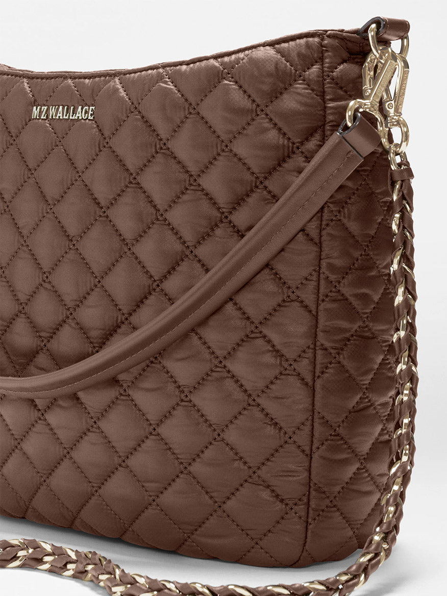Close-up of a brown quilted MZ Wallace Crosby Hobo in Walnut Oxford, featuring Italian leather trim, gold clasp, and chain detailing against a white background.