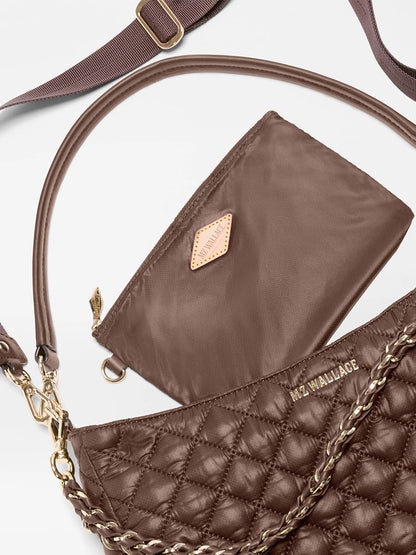 The MZ Wallace Crosby Hobo in Walnut Oxford is a quilted brown handbag crafted from recycled nylon, accented with refined Italian leather trim. It features a gold chain strap, a matching small pouch, and a detachable shoulder strap, with the brand name “MZ WALLACE” displayed on the bag.