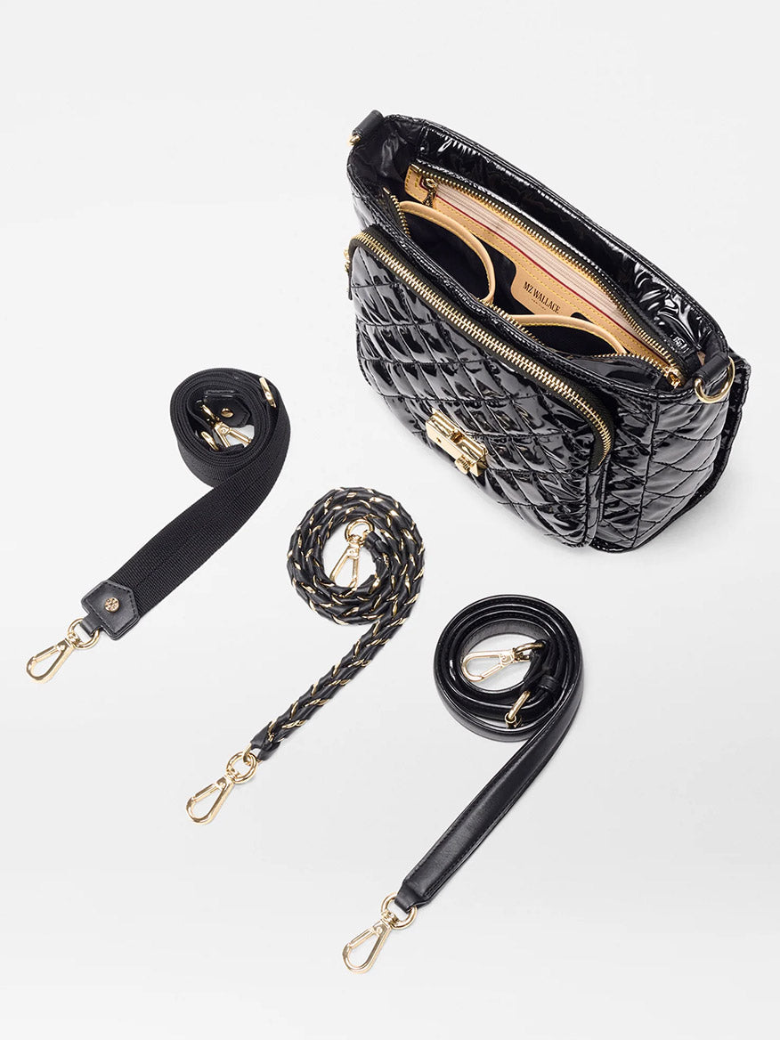 The MZ Wallace Crosby Lock Medium Crossbody in Black Lacquer Oxford features gold hardware, a tan interior, chic lock-and-key closure, and comes with three detachable straps—fabric, braided, and leather—arranged beside the displayed open bag.