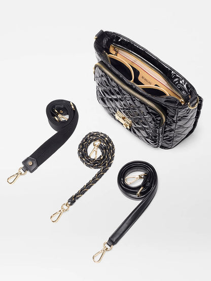 The MZ Wallace Crosby Lock Medium Crossbody in Black Lacquer Oxford features gold hardware, a tan interior, chic lock-and-key closure, and comes with three detachable straps—fabric, braided, and leather—arranged beside the displayed open bag.