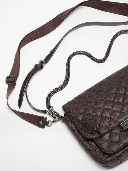 The MZ Wallace Crosby Lock Medium Crossbody in Espresso Oxford, featuring quilted brown leather, a woven chain strap, and an adjustable fabric shoulder strap, is displayed on a white surface.
