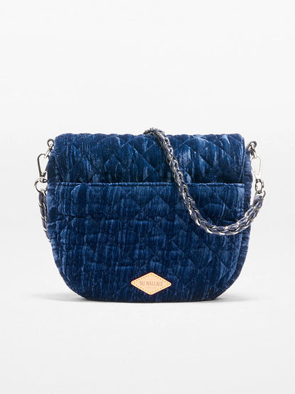 The MZ Wallace Crosby Lock Saddle in Midnight Velvet is a small quilted navy blue velvet crossbody bag with a detachable chain strap and a tan logo patch on the front.