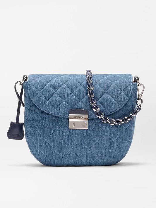 The MZ Wallace Crosby Lock Saddle in True Blue Denim features a blue quilted design, silver-tone chain strap, Italian leather trim, metal clasp closure, and a small leather tag on the side, displayed against a plain background.