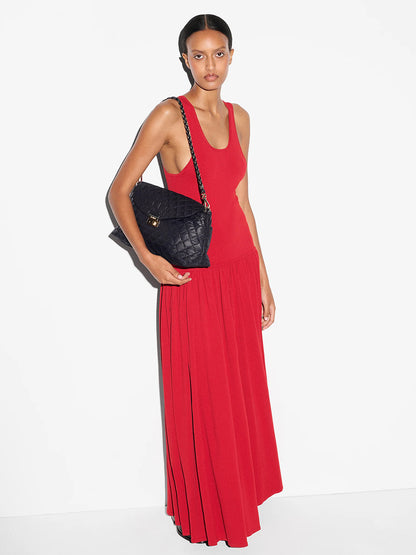 A person in a sleeveless red dress stands against a white background, holding the MZ Wallace Crosby Lock Shoulder in Black Oxford, featuring an Italian leather strap.